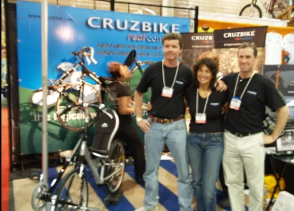 Three people in Cruzbike shirts at an early Cruzbike trade show stand