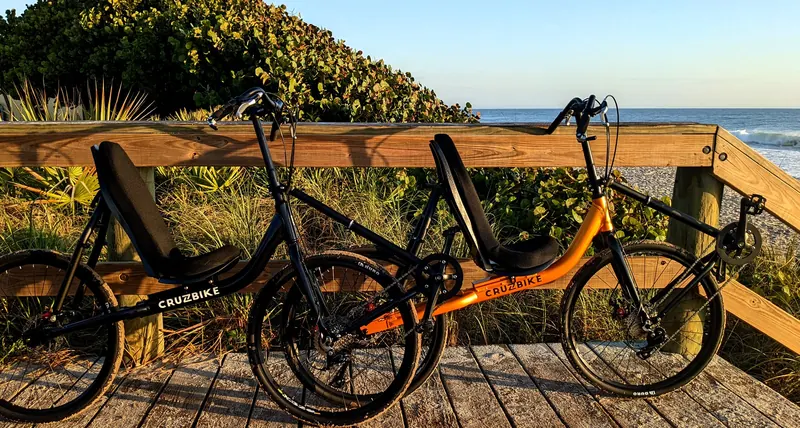 A black and a gold Cruzbike T50 parked on a wooden beach boardwalk at golden hour