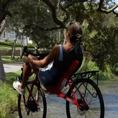 A rider on a red Cruzbike by the water under oak trees