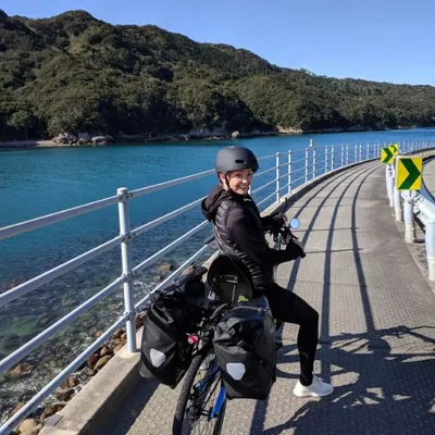 A rider with panniers on a Cruzbike on a seaside path, smiling at the camera